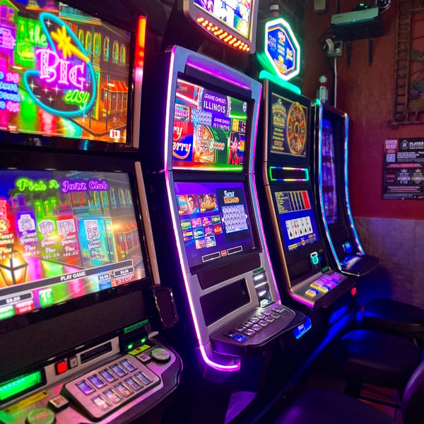 Row of brightly lit slot machines with neon accents, displaying various game screens in a dark room.