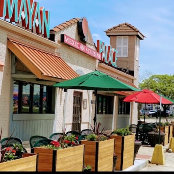 Exterior of Mayan Palace restaurant with outdoor seating under green and red umbrellas.