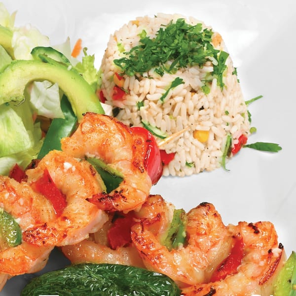 Grilled shrimp skewers with bell peppers, rice pilaf, and a side salad with avocado.