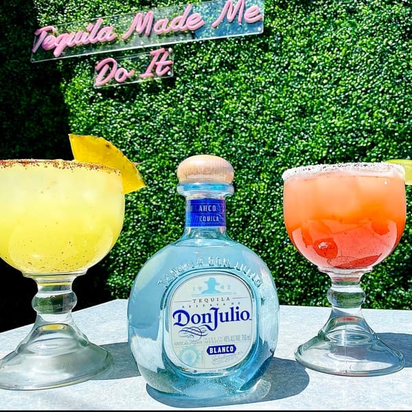 Don Julio tequila bottle between yellow and orange margaritas with a "Tequila Made Me Do It" sign.