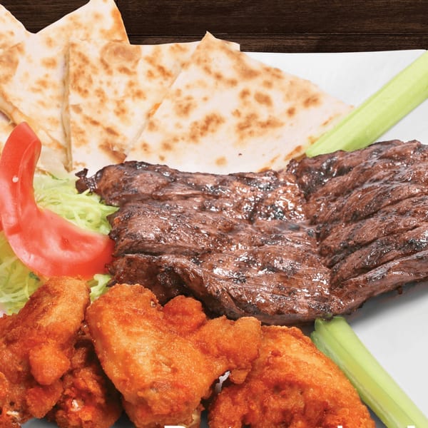 Grilled steak, fried chicken wings, quesadilla wedges, and fresh vegetables on a white plate.