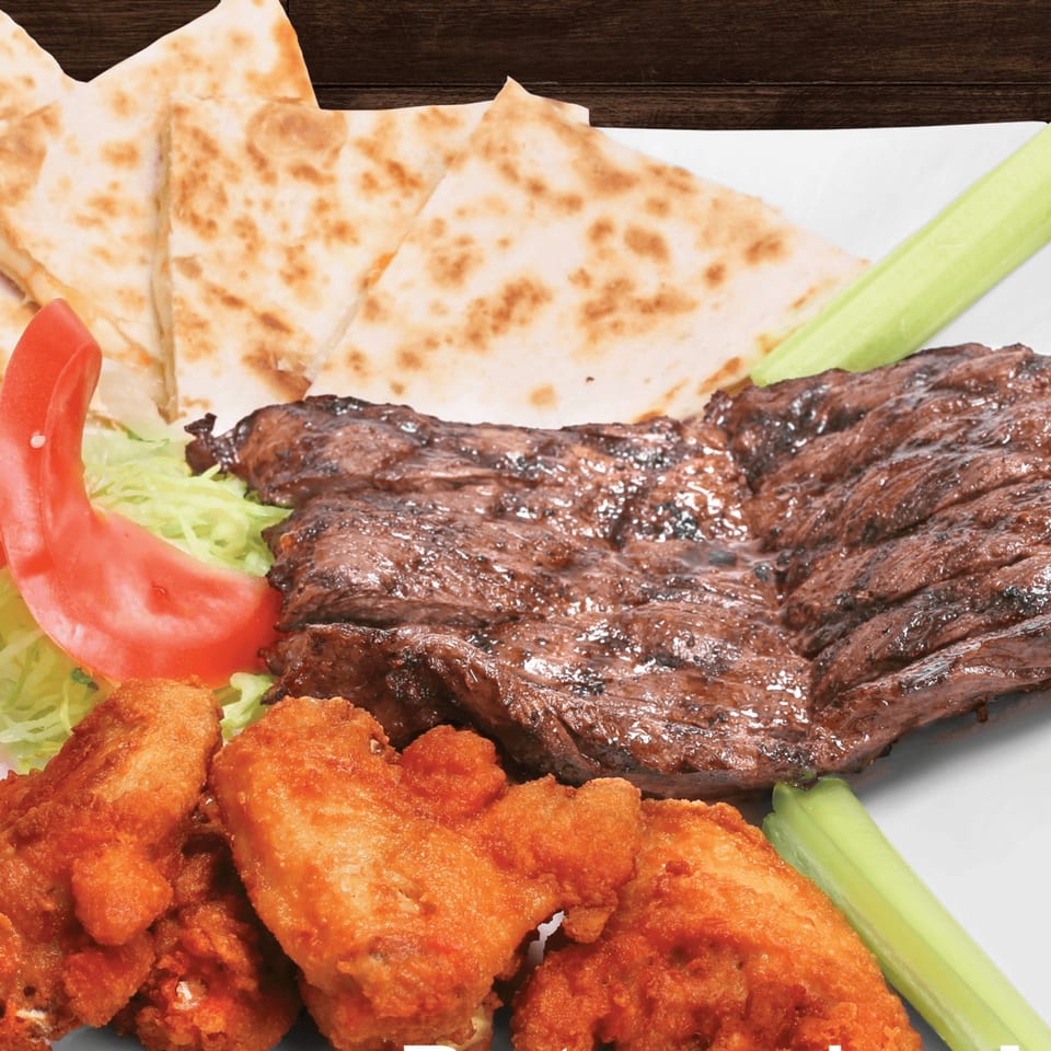 Grilled steak, fried chicken wings, quesadilla wedges, and fresh vegetables on a white plate.