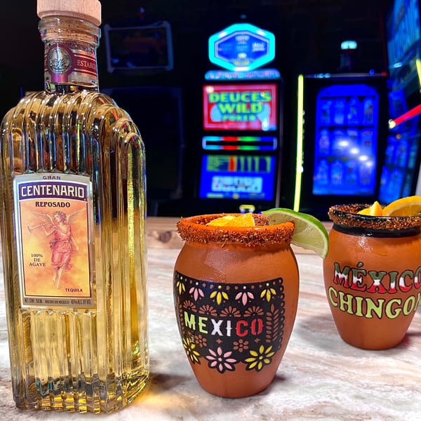 A bottle of Gran Centenario Reposado tequila next to two Mexican clay cups with fruit slices.