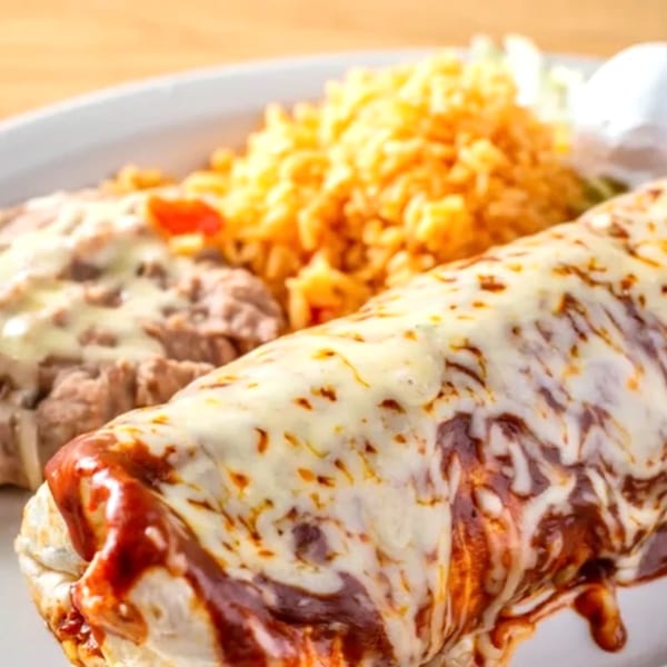A Mayan Palace burrito covered in melted cheese and red sauce, with rice and refried beans.