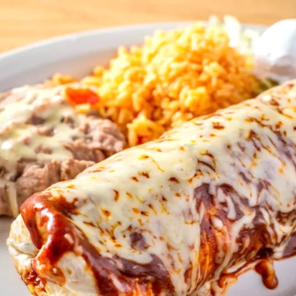 A Mayan Palace burrito covered in melted cheese and red sauce, with rice and refried beans.