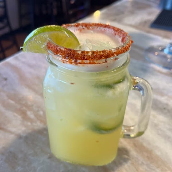 A Mayan Palace margarita in a mason jar, garnished with a lime wedge and chili-salt rim.