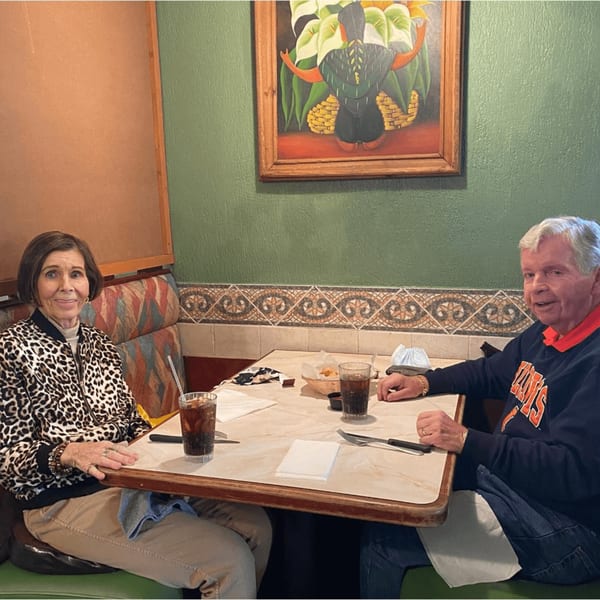 Two people, a woman and a man, sitting at a table in a Mayan Palace restaurant, with drinks and chips.