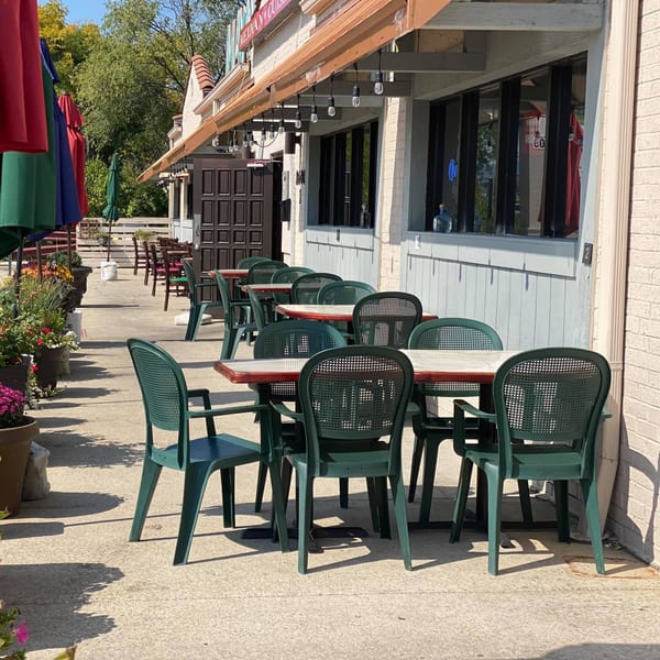 Outdoor patio of Mayan Palace with green chairs, tables, colorful umbrellas, and potted plants.