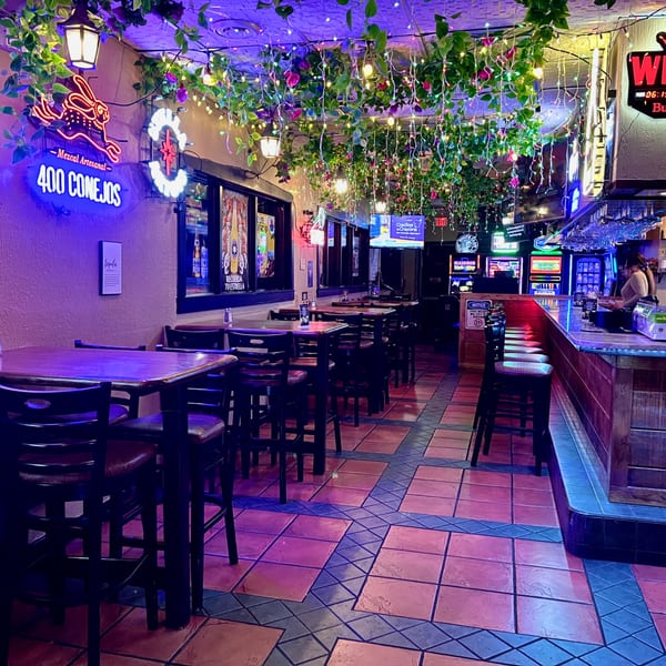 Interior of Mayan Palace, a Mexican restaurant, with neon signs, bar, tables, and vine decorations.